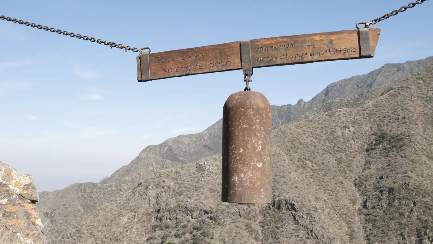 Campana colgada de una viga de madera, con la montaña de fondo