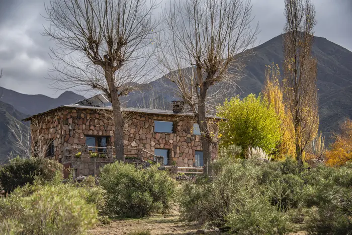Casa de piedra entre álamos y arbustos, con la montaña de fondo