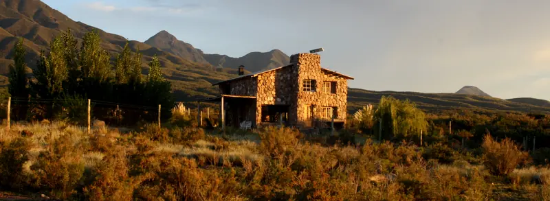Casa de piedra al amanecer, rodeada de jarilla y montaña