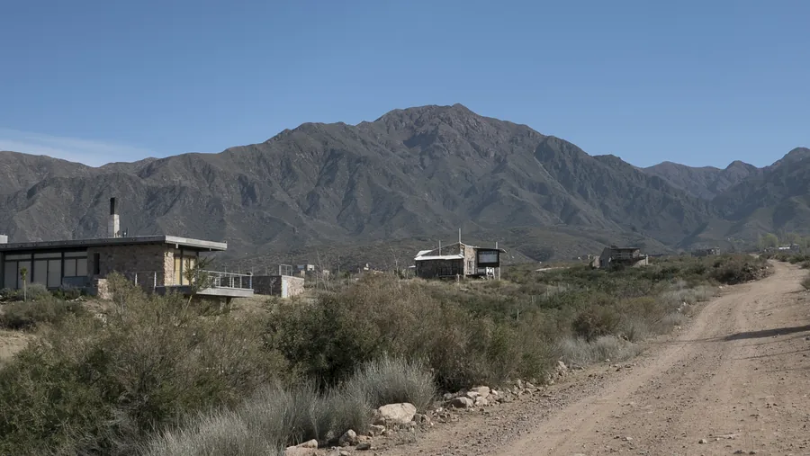 Casas de piedra y vidrio junto a una calle de tierra, con la montaña de fondo