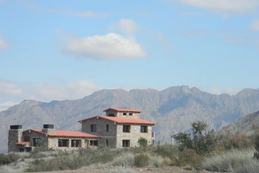 Casa de piedra de dos plantas con techos de tejas, frente a la montaña