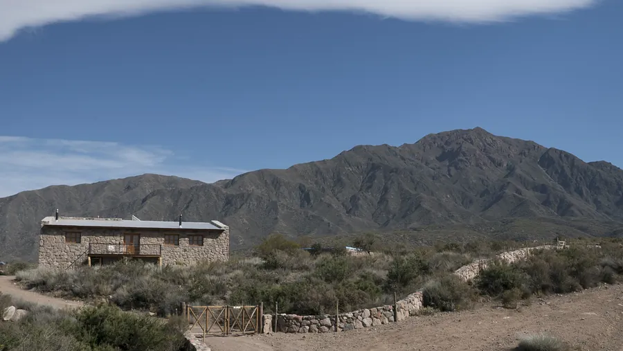 Casa de piedra alargada frente a la montaña, con pirca y tranquera de madera