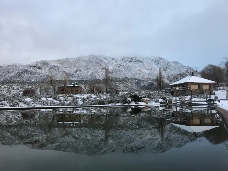 Dos casas de piedra y la montaña nevada, reflejadas en el agua