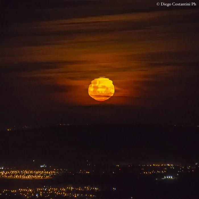 Luna anaranjada entre nubes, sobre las luces de la ciudad