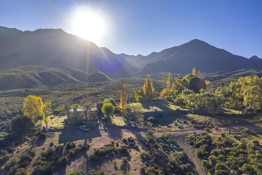 Vista aérea de álamos dorados y una casa del barrio, con el sol sobre la montaña